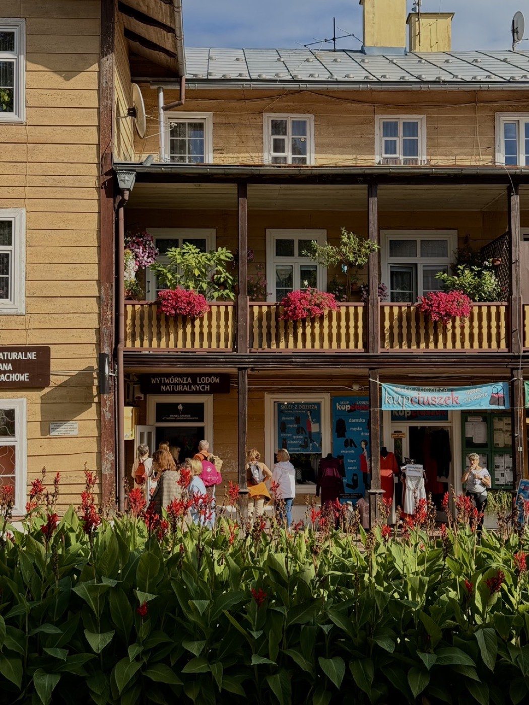 Drewniany budynek z galerią na piętrze, na parterze lodziarnia z kolejką