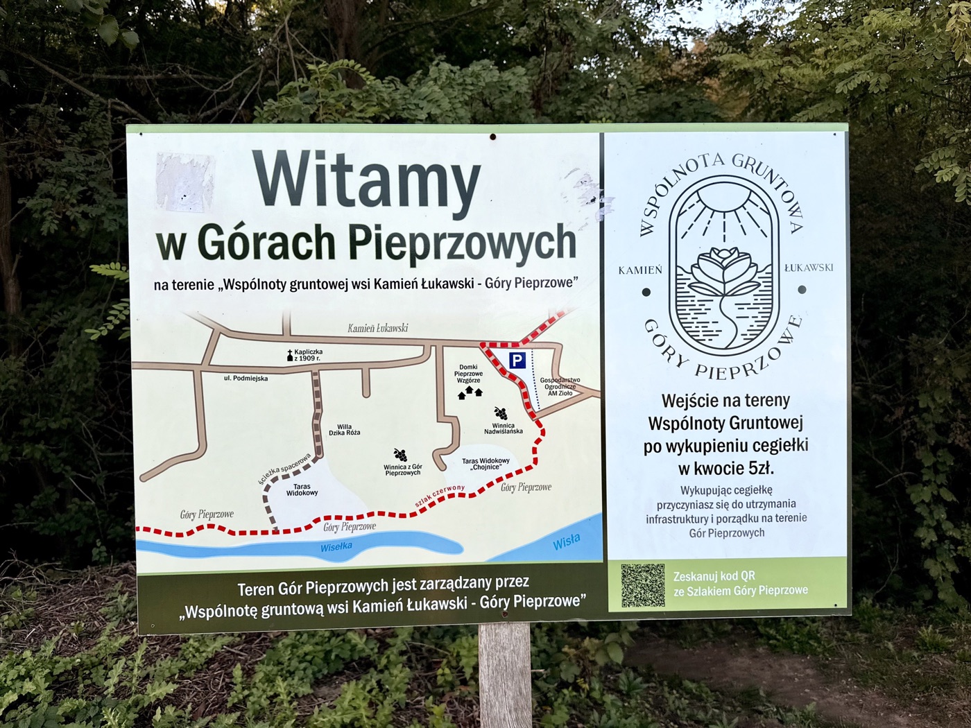 Tablica na drewnianym słupku z powitaniem w Górach Pieprzowych, uproszczoną mapą z czerwonym szlakiem, tarasami widokowymi i winnicami, informacją o cegiełce i kodem QR